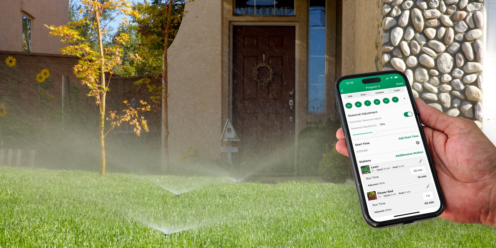 Hand holding a phone while lawn sprinklers operate in front of a house.