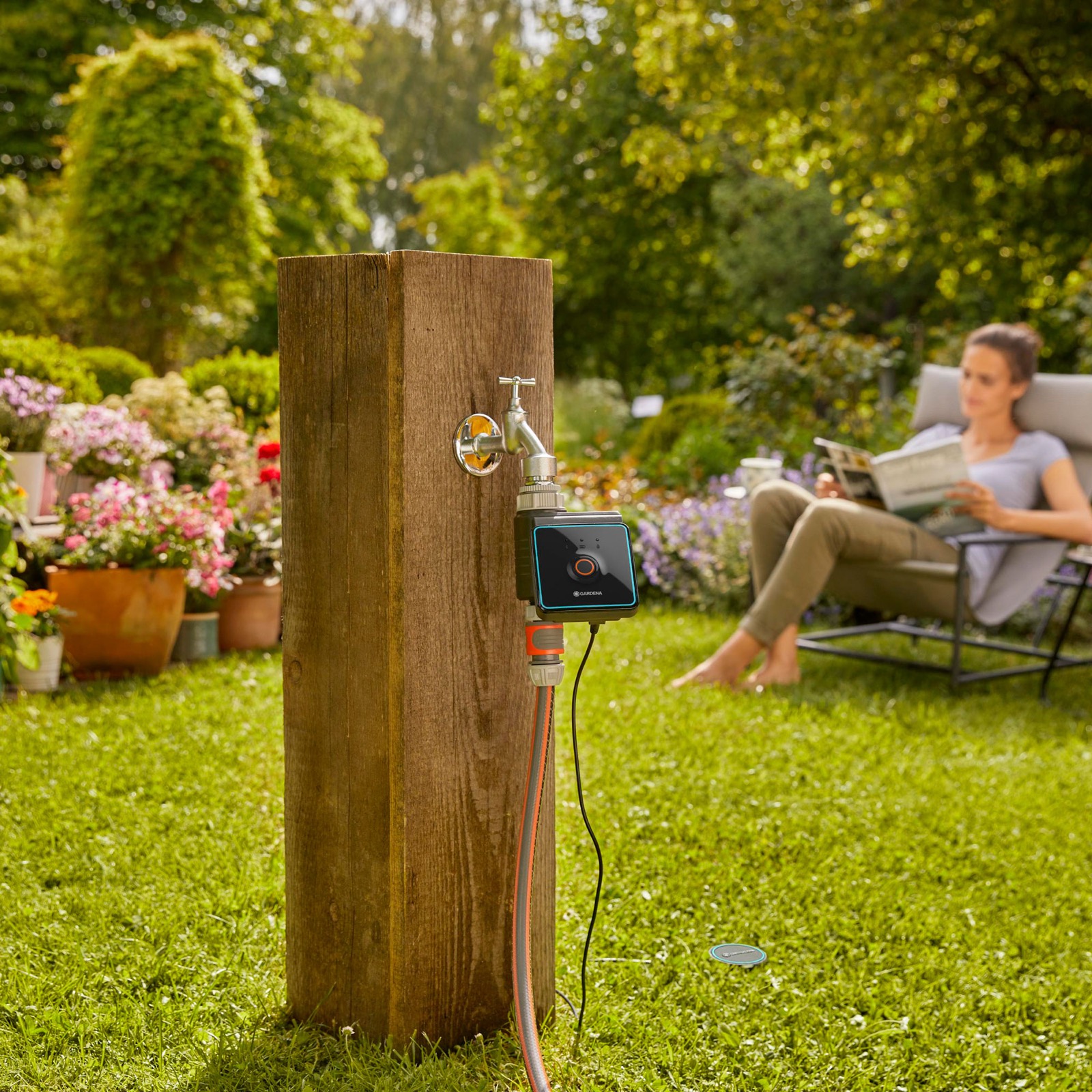 Outdoor tap column with a watering controller attached in a landscaped home garden.